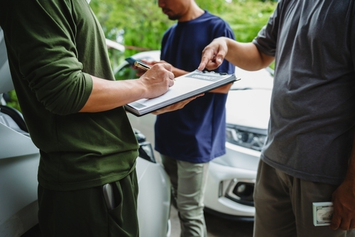 Michigan car accident lawyer image of people signing accident report paperwork next to a damaged vehicle
