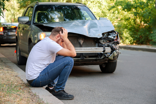 Michigan car accident lawyer image of driver sitting in distress beside heavily damaged car after a crash