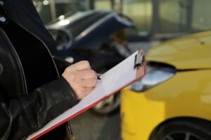 Michigan car accident lawyer police report image of person writing accident details on clipboard near damaged car