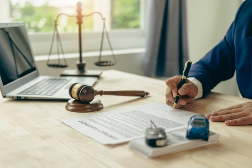 Michigan car accident lawyer image of attorney signing legal paperwork with gavel and car model representing accident claim