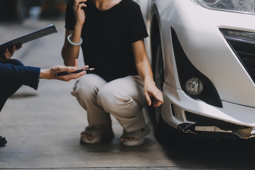 Michigan car accident lawyer image of driver inspecting vehicle damage and documenting evidence after a crash
